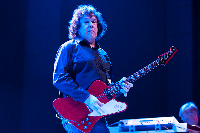 Gary Moore playing a red Firebird guitar on a blue-lit stage during a 2009 concert.